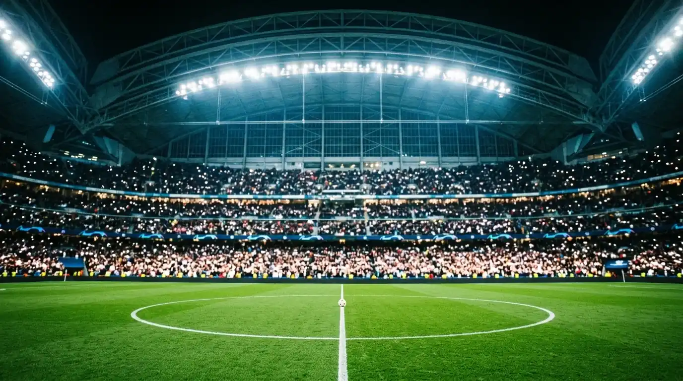 Grosses Fussballstadion mit geschlossenem Dach bei Flutlicht, grüner Rasen im Vordergrund mit Anstosskreis, gefüllte Ränge